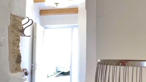 A hallway with a door leading to an outdoor area, a ceiling fan, and a fruit bowl on a counter. - The Cliffs - La Maison du Puits (Porto do Barqueiro)