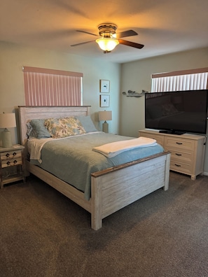 A bedroom with a bed, a ceiling fan, a TV, a nightstand, and a dresser. - Beautiful Pool home on Canal! (Saint James City)