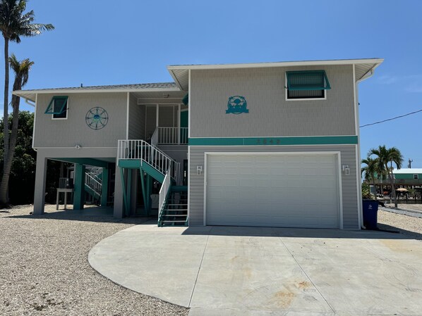 A two-story building with a garage, a staircase, and a small outdoor seating area. - Beautiful Pool home on Canal! (Saint James City)
