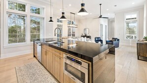 Cozinha moderna com ilha grande, eletrodomésticos de aço inoxidável e iluminação pendente.