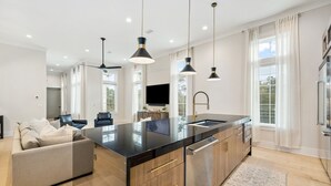 Uma cozinha moderna com ilha central, eletrodomésticos de aço inoxidável e iluminação pendente.