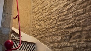 A staircase with a textured stone wall, a red handrail, and black and white patterned steps. - Bâtisse du Xixe, Ranville (Ranville)