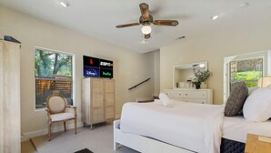 Un dormitorio moderno con cama, una silla, armario, ventilador de techo y televisor que muestra servicios de streaming.