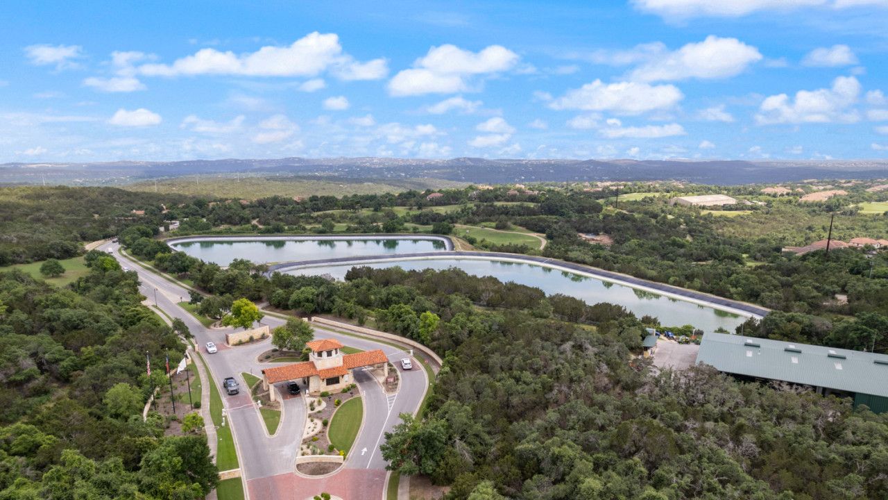 An aerial view of a property with a curved road, a central building with a red roof, and surrounding greenery.