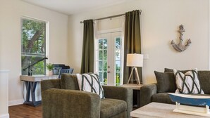 Una sala de estar con dos sillones verdes, una mesita con una lámpara y un escritorio con una computadora.