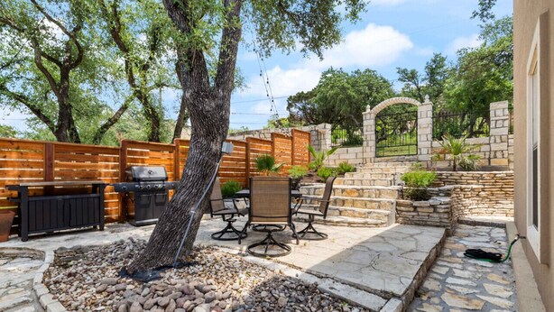 Un patio al aire libre con suelo de piedra, valla de madera, pared de piedra y una parrilla.