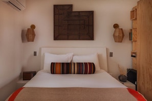 Un dormitorio con una cama, una obra de arte colgada en la pared, una mesita de noche y un buró.