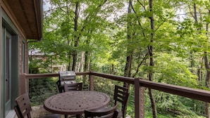 A balcony with a round table and chairs, overlooking a forested area. - Altitudes Attitude (Blowing Rock)