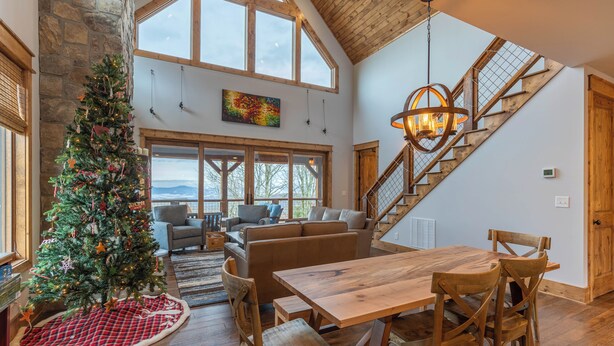 A spacious living area with a wooden dining table, a Christmas tree, and a staircase leading to an upper level. - Neverending Story at Eagles Nest (Elk Park)