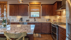 A kitchen with wooden cabinets, a granite countertop, stainless steel appliances, and a hanging light fixture. - Neverending Story at Eagles Nest (Elk Park)