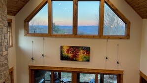 A spacious room with a high ceiling, large windows offering a view of the mountains, a stone wall, and a painting on the wall. - Neverending Story at Eagles Nest (Elk Park)
