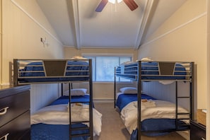 Um quarto de dormitório com beliches, cômoda e ventilador de teto.