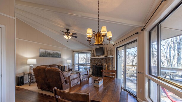 A spacious dining area with a wooden table and chairs, a fireplace, and large windows offering a view of the outdoors. - Sugar Mountain Serenity (Banner Elk)