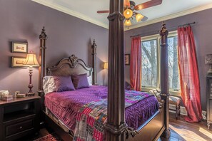 A four-poster bed with a purple bedspread, a nightstand with a lamp, and a window with red curtains. - View House (Boone)