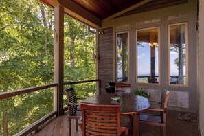 A wooden deck with a round table and chairs, large windows, and a view of trees. - View House (Boone)