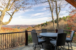 A covered outdoor patio with a round table and four chairs, overlooking a scenic view of autumn foliage and distant hills. - Bailey's Creek Lodge (Lenoir)