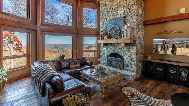 Ein geräumiges Wohnzimmer mit Kamin aus Stein, großen Fenstern mit herrlichem Ausblick, einer Ledersofa und einem Couchtisch.