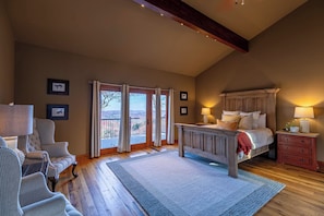 A bedroom with a large bed, a wooden headboard, a nightstand, a chair, and a view through the glass doors. - Bailey's Creek Lodge (Lenoir)