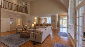 A spacious living room with a high ceiling, a large sofa, a coffee table, and a staircase leading to an upper level. - Mountain Gem (Boone)