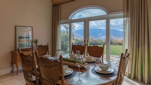 A dining area with a table set for four, wooden chairs, and a view of mountains through large windows. - Mountain Gem (Boone)