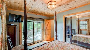 A four-poster bed with a patterned bedspread, a television mounted on the wall, and a wooden ceiling. - Crystal View (Boone)