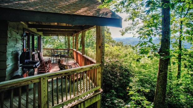 A wooden cabin with a porch, outdoor seating, and a view of a forested landscape. - Crystal View (Boone)