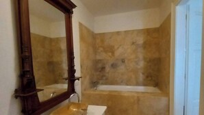 A bathroom with a stone wall, a white sink, a large mirror, and a bathtub. - Antique Old Town Apartment (Prague)