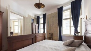 A bedroom with a large bed, wooden headboard, a hanging light fixture, and a view of a cityscape through the window. - Antique Old Town Apartment (Prague)