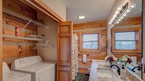 Une salle de bain moderne et compacte, avec un intérieur en bois, un lave-linge, un lavabo doté d’un plan de travail en marbre et un grand miroir.