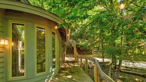 Una terraza de madera que conduce a una casa con ventanas grandes, rodeada de árboles.