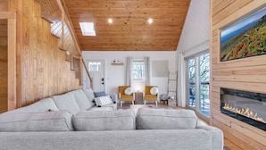 A cozy living room with a grey sofa, wooden ceiling, and a fireplace. - Calling Me Home (Lenoir)