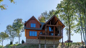 A two-story wooden house with a stone foundation, a balcony, and a stone retaining wall. - Evergreen at Eagles Nest (Elk Park)
