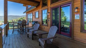A wooden deck with Adirondack chairs, a grill, and a scenic view of hills. - Evergreen at Eagles Nest (Elk Park)