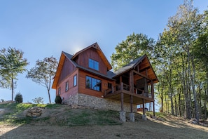 A two-story wooden cabin with a stone foundation, large windows, and a balcony. - Evergreen at Eagles Nest (Elk Park)