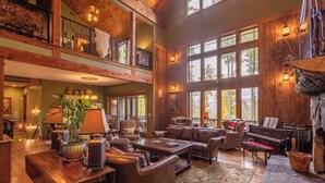 A spacious, multi-level living area with wooden floors, leather furniture, and large windows offering views of the outdoors. - Homestead Lodge at Eagles Nest (Banner Elk)
