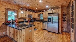 A wooden cabin interior with a kitchen featuring a central island, stainless steel appliances, and wooden cabinetry. - 1 Awesome Skyview (Vilas)