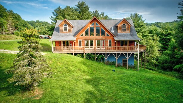 A log cabin with a covered porch and a deck, surrounded by lush greenery. - 1 Awesome Skyview (Vilas)