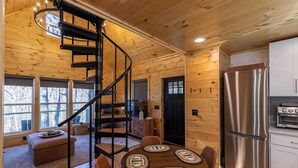 A cabin interior with a spiral staircase, wooden walls, a dining area with round tables, and a kitchen with stainless steel appliances. - Retreat at Riverbend (West Jefferson)