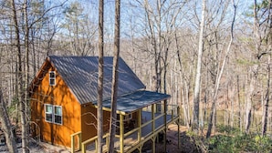 A cabin with a metal roof, wooden deck, and surrounded by trees. - Retreat at Riverbend (West Jefferson)