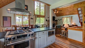 A kitchen with a stainless steel range, a built-in oven, and a stone fireplace. There are large windows offering views of the outdoors. - Sunrise with Grandfather (Banner Elk)