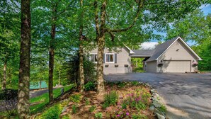A two-story house with a garage, surrounded by mature trees and a landscaped garden with various plants and flowers. - Sunrise with Grandfather (Banner Elk)