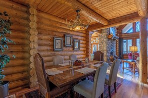 L’intérieur d’une cabane en rondins, avec une table à manger, des chaises, un lustre, des tableaux encadrés et une cheminée en pierre.