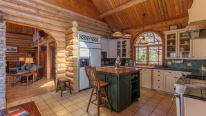 Interior de una cabaña de troncos con cocina, comedor y chimenea.