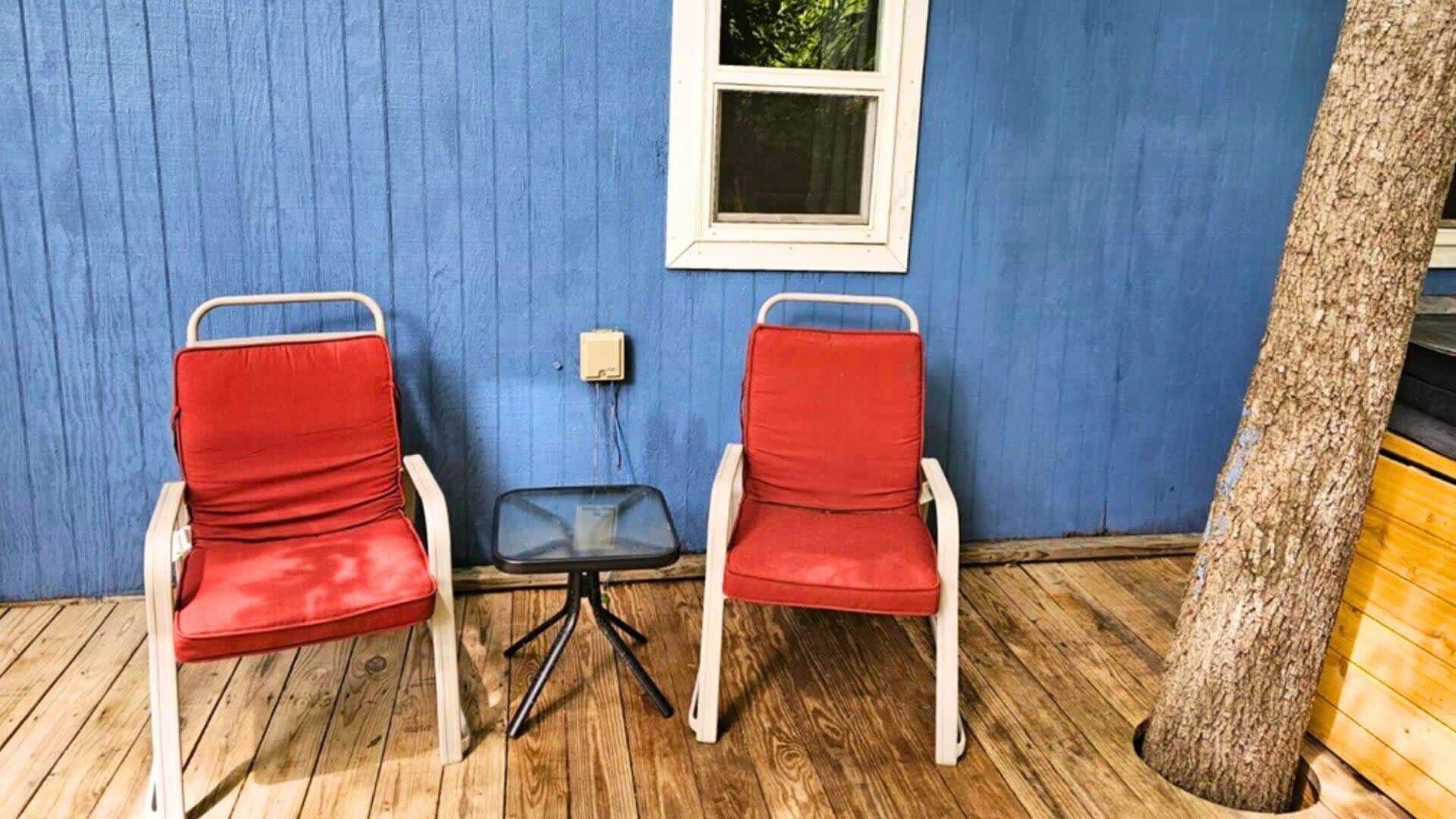 Twee rode stoelen met witte frames en een kleine tafel voor een blauwe muur met een raam.