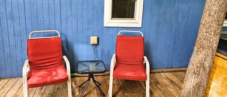 Twee rode stoelen met witte frames en een kleine tafel voor een blauwe muur met een raam.