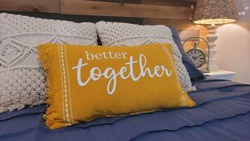 Una cama con colcha azul, una manta tejida blanca y una almohada amarillo mostaza con el texto 'better together'.