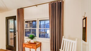 A room with a wooden floor, a white chair, a small table with a plant, and a window with curtains. - Orchid Cabin (Banner Elk)