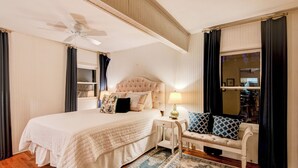 A bedroom with a large bed, a nightstand, a bench, a ceiling fan, and a window with curtains. - Orchid Cabin (Banner Elk)