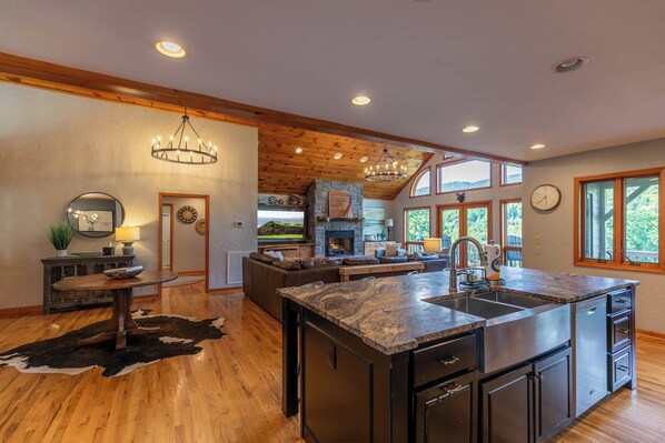 A spacious kitchen with a large island, wooden ceiling beams, and a stone fireplace. - Boulder Sky at River Run (Banner Elk)