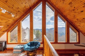 A cozy attic room with a large skylight, a rocking chair, and a view of the surrounding landscape. - New River Retreat (Boone)